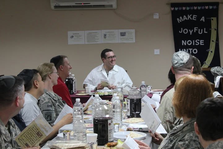 Ephraim Travis in a white kittel leading a Passover Seder for soldiers seated around a long table in Iraq