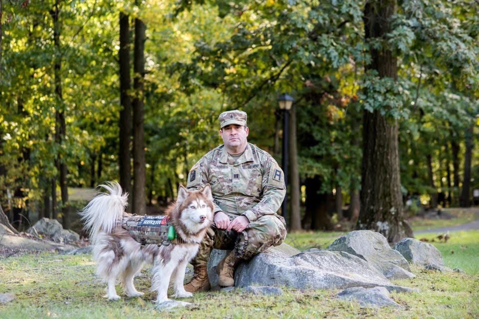 Ephraim Travis in Army uniform, seated on a rock in autumn woods with a husky beside him