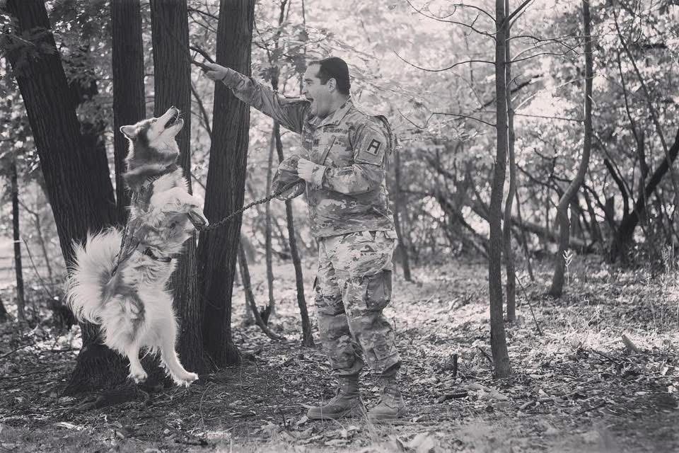 Black-and-white photo of Ephraim Travis playing with a husky in the woods